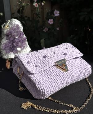Handmade lavender crochet shoulder bag studded with amethyst beads, with a gold clasp and gold chain strap, beside an amethyst geode