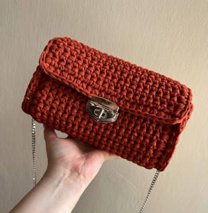 Handmade terracotta crochet crossbody bag with a gold clasp and chain strap, held in hand